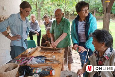 Szuhankó Sándor az érdeklődő hölgykoszorúban oktatja a gyékényszövés fortélyait (Kazinczy Paszterkó Diana felvétele)