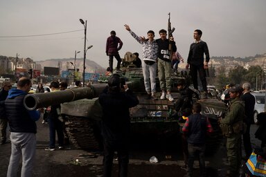 Suhancok felkelőktől kölcsönkért karabélyokkal fényképezkednek a kormányerők hátrahagyott tankján Damaszkusz terén (Fotó: AP via Beta)