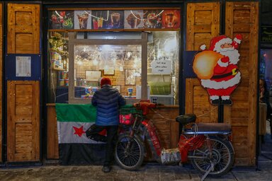 Várakozás egy karácsonyi ünnepekre feldíszített gyümölcsléstand előtt Damaszkuszban/AP via Beta