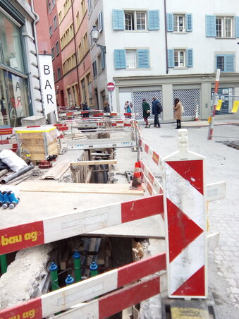 Vízvezetékcsere Zürich belvárosában. A csövek legalább százévesek, valóban cserére érettek, és nem csak azért cserélik őket, mert „most van meg rá a keret”, vagy mert valamelyik cégnek „kell a meló”. A helybeliek a megszokott utakon közlekednek, az árkok fölé több helyen hidacskákat tesznek, hogy ne kelljen keringeniük. A „hidacskás” megoldást Újvidéken is alkalmazták, még 15 évvel ezelőtt is az úttestet átszelő árkok fölé kora délután, az aznapi meló elvégeztével a munkások 2-3 cm vastag acéllapokat húztak, így másnap reggelig autóval is közlekedhettünk az építkezés területén. Ilyesmit már nagyon régen nem láttunk sehol. Bocsánat, Zürichben láttunk.