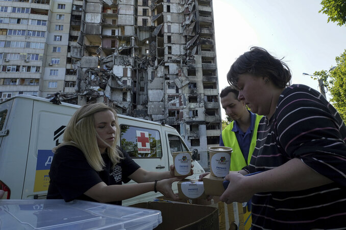 Volontőrök ételt osztanak a háttérben látható megrongált harkivi épület lakóinak (Fotó: AP via Beta)