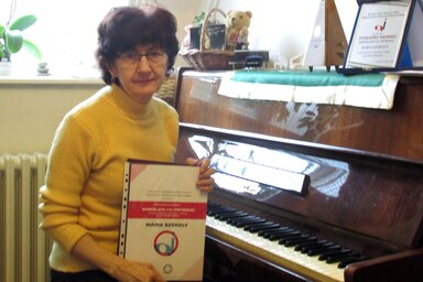 A tanárnő a díjai és a zongorája mellett