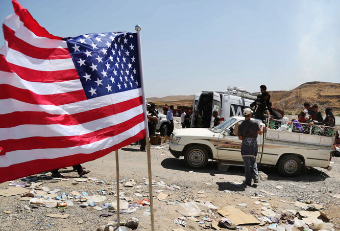 Amerikai lobogót lenget a szél a szír–iraki határon, miközben menekült jazidik kelnek át a Tigrisen átívelő hídon (Fotó: Beta/AP)