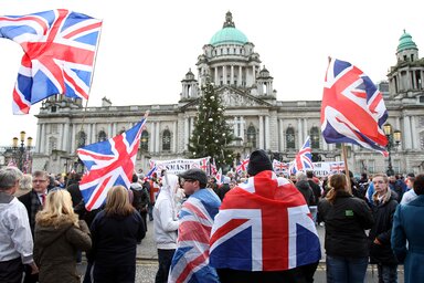 Brit lobogókat lengető protestánsok csoportjai tüntetnek a belfasti városháza előtt, amiatt, hogy a – katolikus többségű – városi parlament a városházáról levetette a brit zászlót