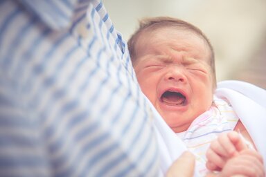 Baby crying in mother embrace. Newborn and infant healthy concept. Birthday and love of mother theme.