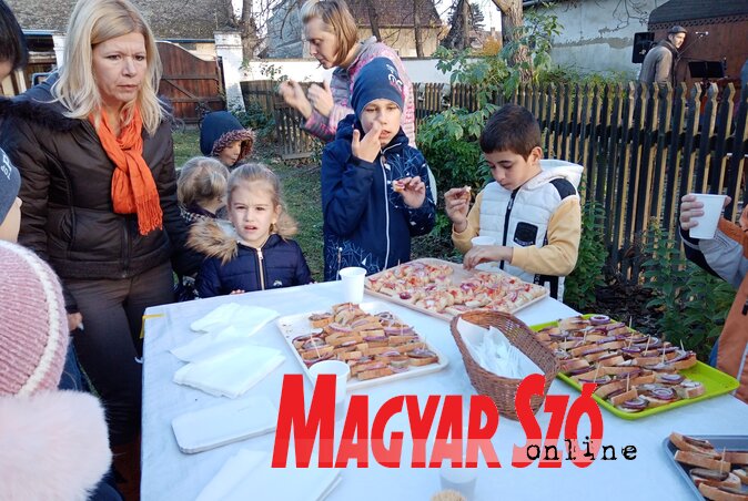 Csípe Tímea ellenőrzi, hogy ízlik-e a gyerekeknek a libapecsenye és a libazsíros kenyér lila hagymával, a háttérben a Juhász zenekar hangol (Fotó: Kazinczy Paszterkó Diana felvétele)